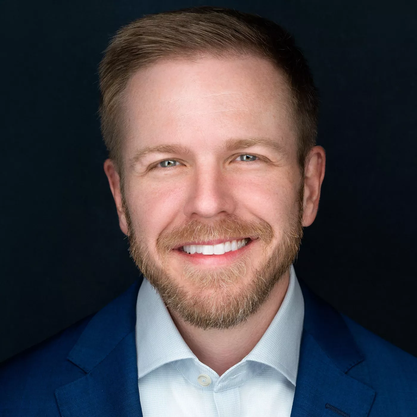 A professional male figure dressed in a tailored blue suit and crisp white shirt. The background is a solid dark tone, emphasizing the formal attire. The image conveys a corporate or business-oriented mood with clean and sharp visuals.